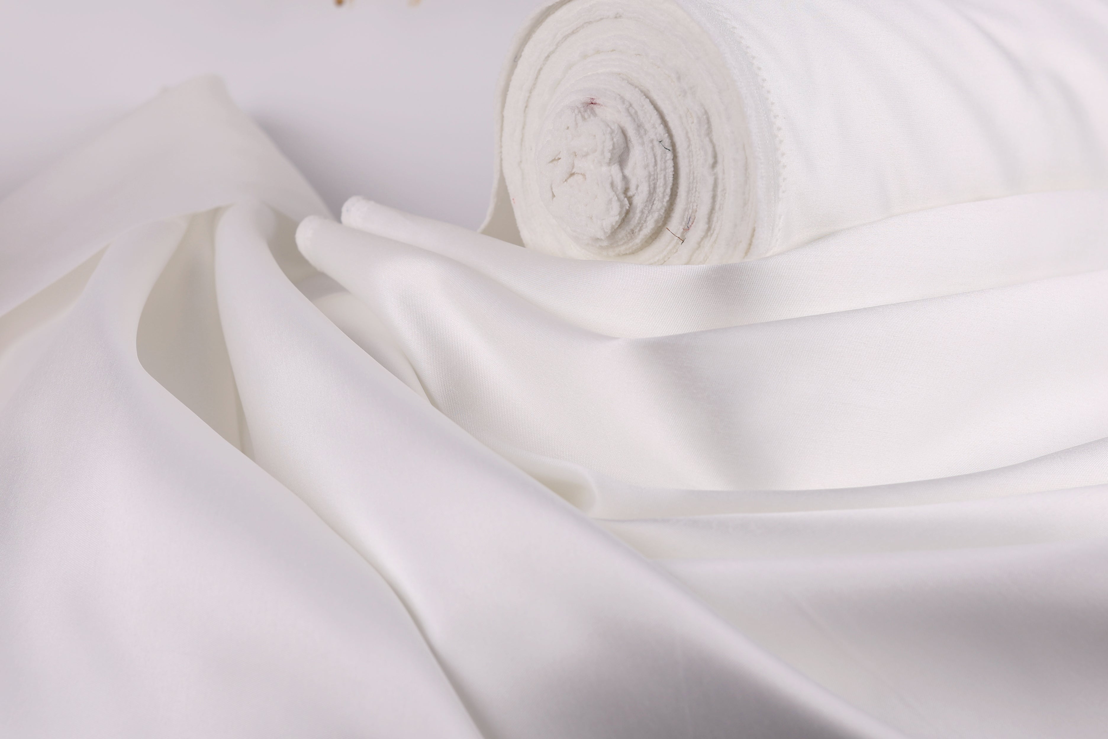A close-up view of a white fabric, possibly silk or satin, with a rolled-up end visible.