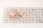 two delicate pink flowers with leaves, placed on a transparent ruler.