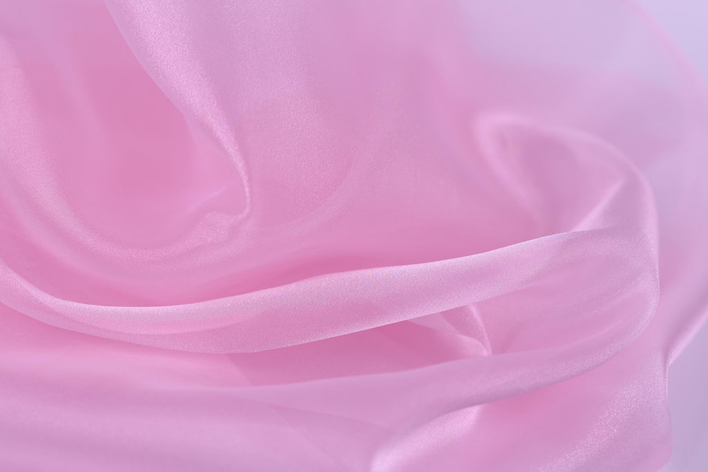 The image is a close-up of a soft, flowing pink fabric, possibly silk or satin, with a smooth and shiny texture.