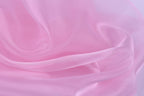 The image is a close-up of a soft, flowing pink fabric, possibly silk or satin, with a smooth and shiny texture.
