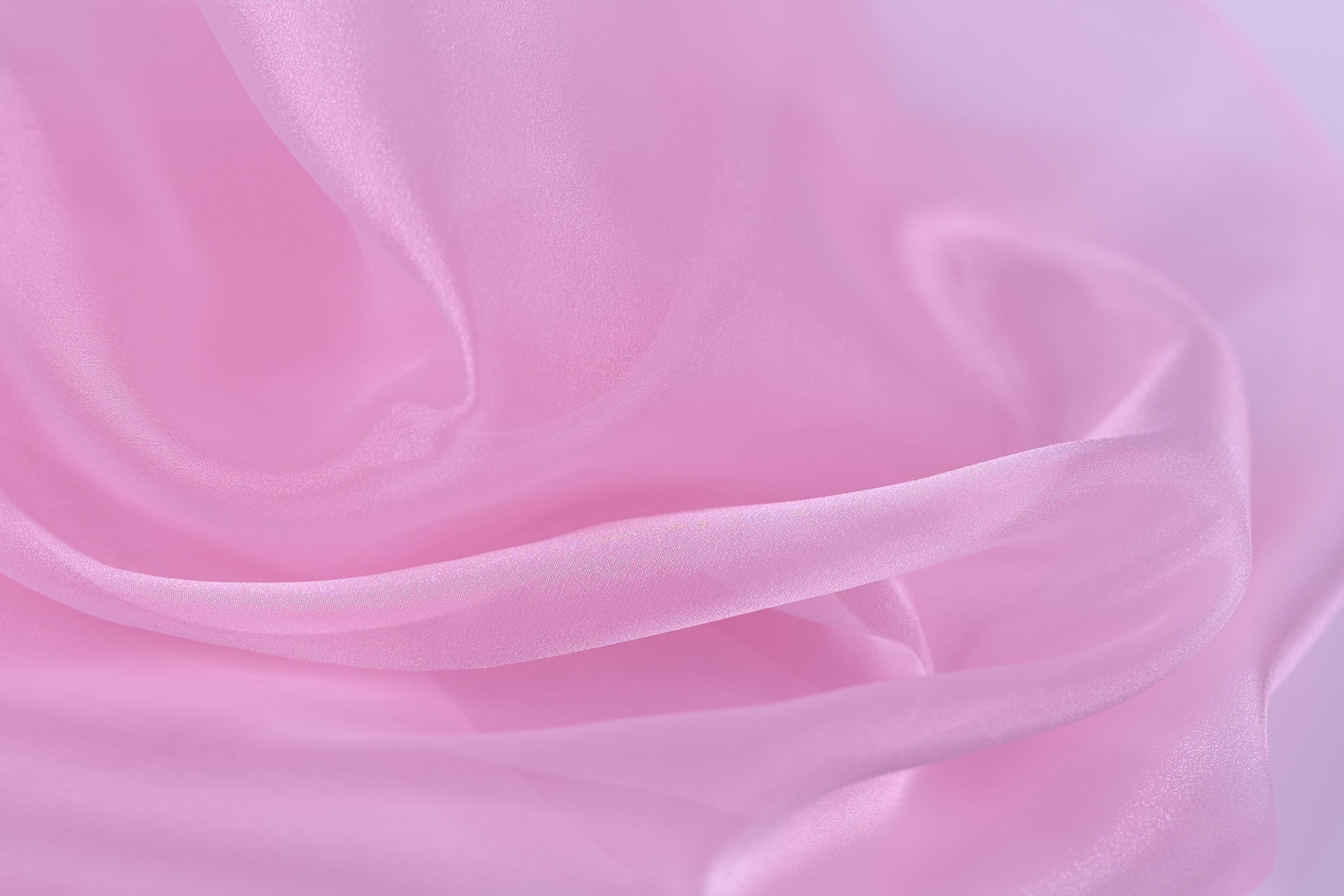 The image is a close-up of a soft, flowing pink fabric, possibly silk or satin, with a smooth and shiny texture.