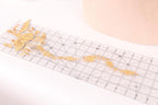 a clear ruler with a decorative gold floral pattern on it, placed on a white surface.