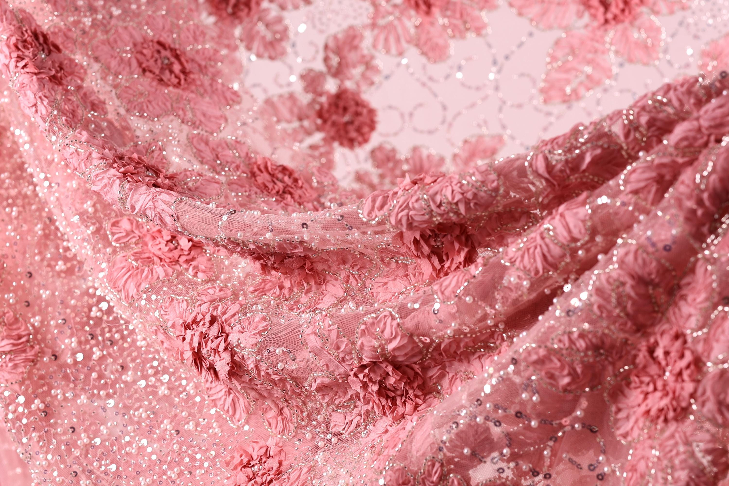 The image is a close-up of a fabric with a pink floral pattern, featuring numerous small pink flowers and sequins or glitter.