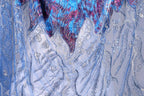 The image is a close-up view of a fabric with a blue and silver pattern, featuring a mix of metallic and floral elements. The fabric appears to be made of a shiny, sequined material, giving it a sparkling and luxurious appearance.