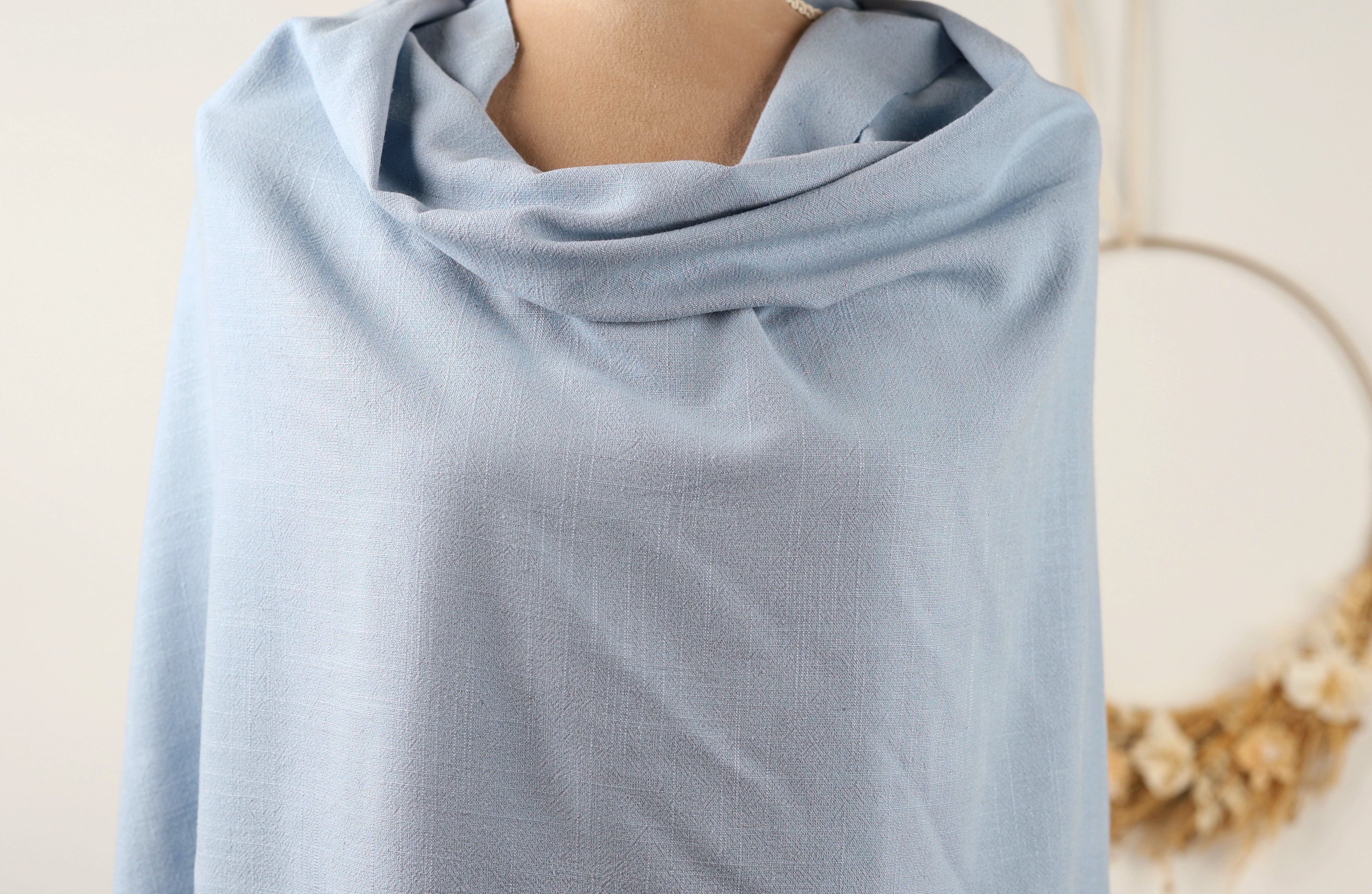 A light blue fabric draped over a mannequin, with a wreath visible in the background.