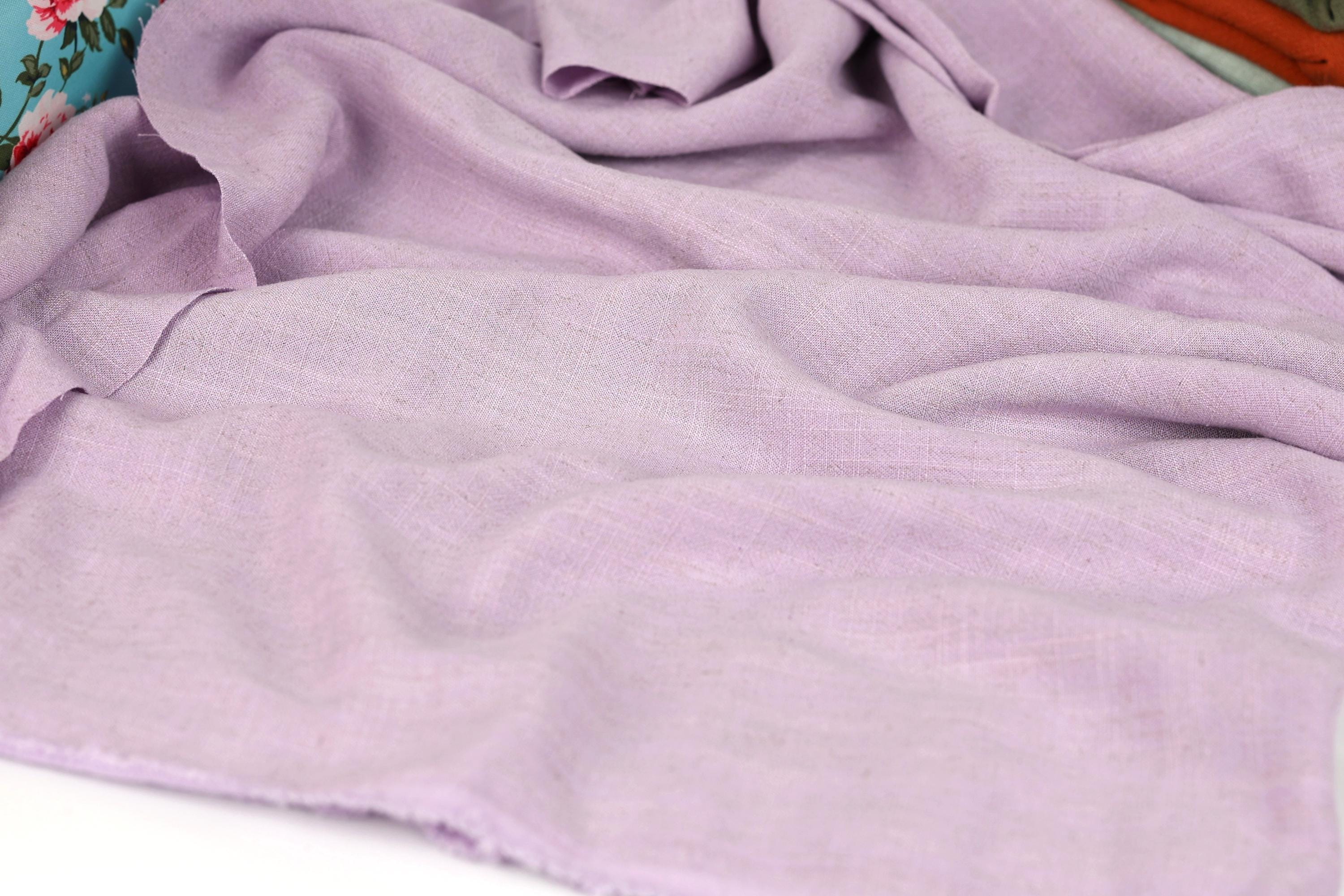 a close-up view of a soft, light purple fabric, possibly a piece of clothing or textile. The fabric appears to be made of a natural, organic material, and it has a slightly wrinkled texture, giving it a relaxed and comfortable appearance.