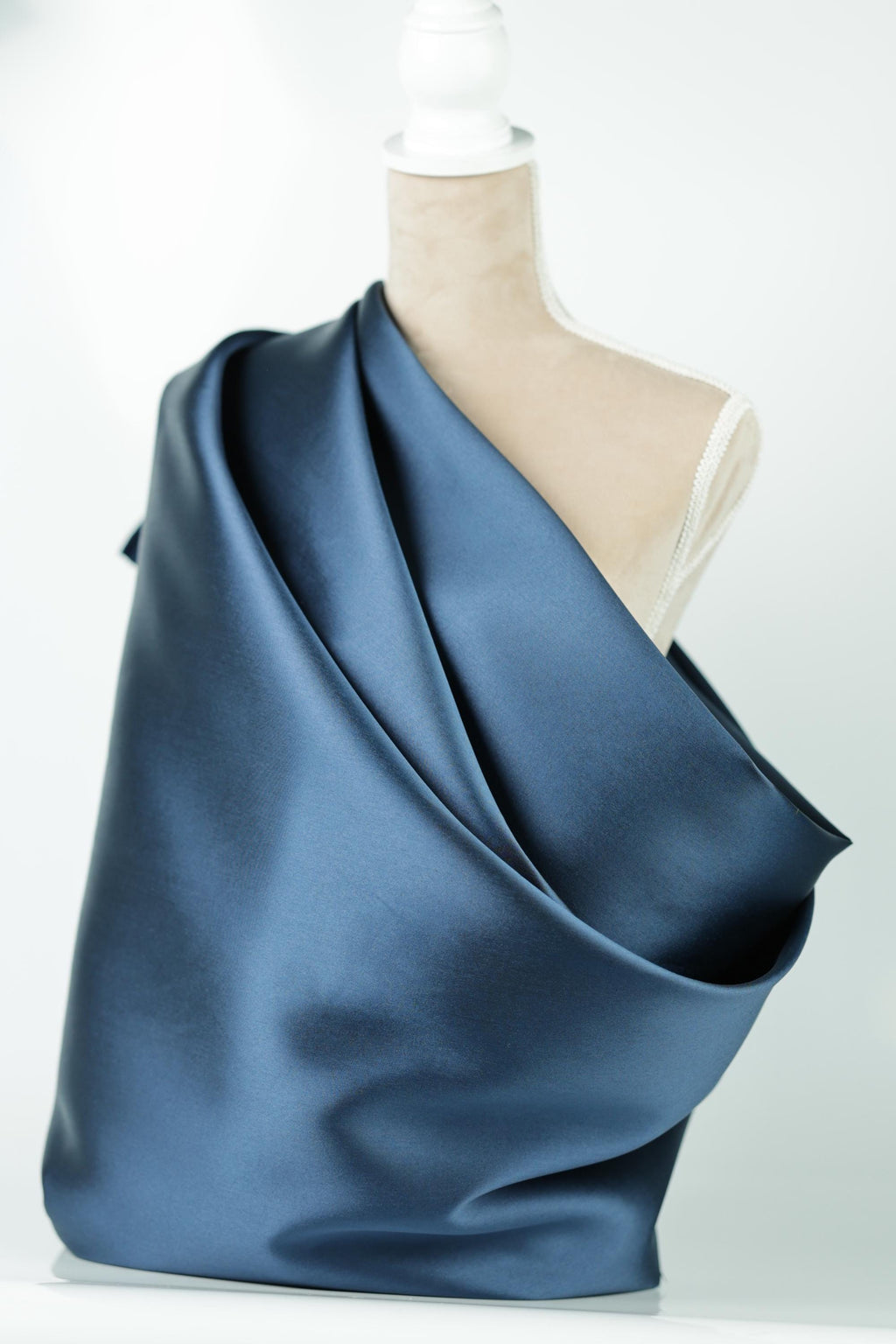A close-up view of a blue satin fabric draped over a white surface, with a person's foot partially visible underneath the fabric.