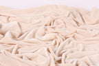 The image is a close-up of a crumpled, light pink fabric, possibly velvet, with a soft, wrinkled texture.