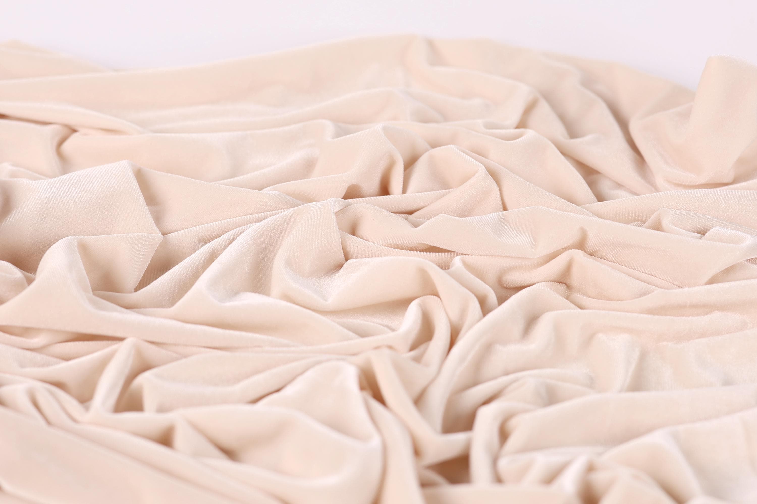 The image is a close-up of a crumpled, light pink fabric, possibly velvet, with a soft, wrinkled texture.