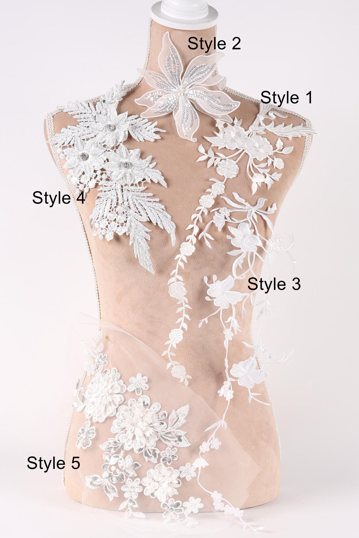 A mannequin with various white lace and floral embroidery pieces attached to it, each with a different style number.