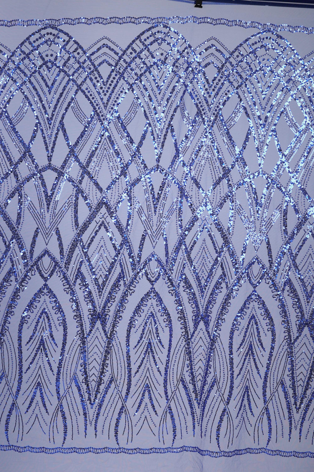a close-up view of a fabric with a repeating pattern of blue sequin designs. The pattern consists of various shapes and lines, creating a visually striking and intricate design. The fabric appears to be a close-up of a piece of clothing or textile, showcasing the detailed craftsmanship and attention to detail in the design.