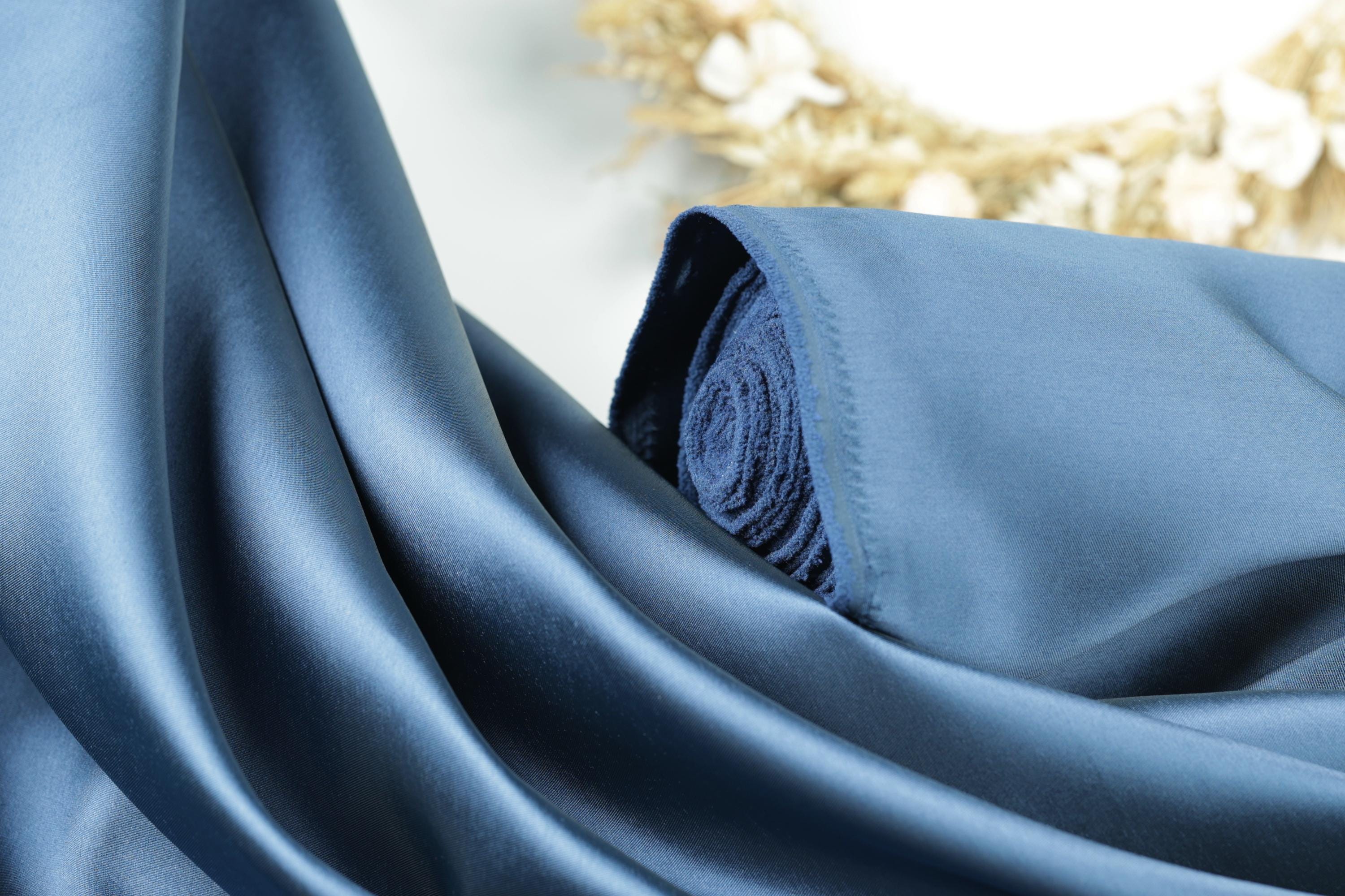 A close-up view of a blue satin fabric, with a rolled-up end visible.
