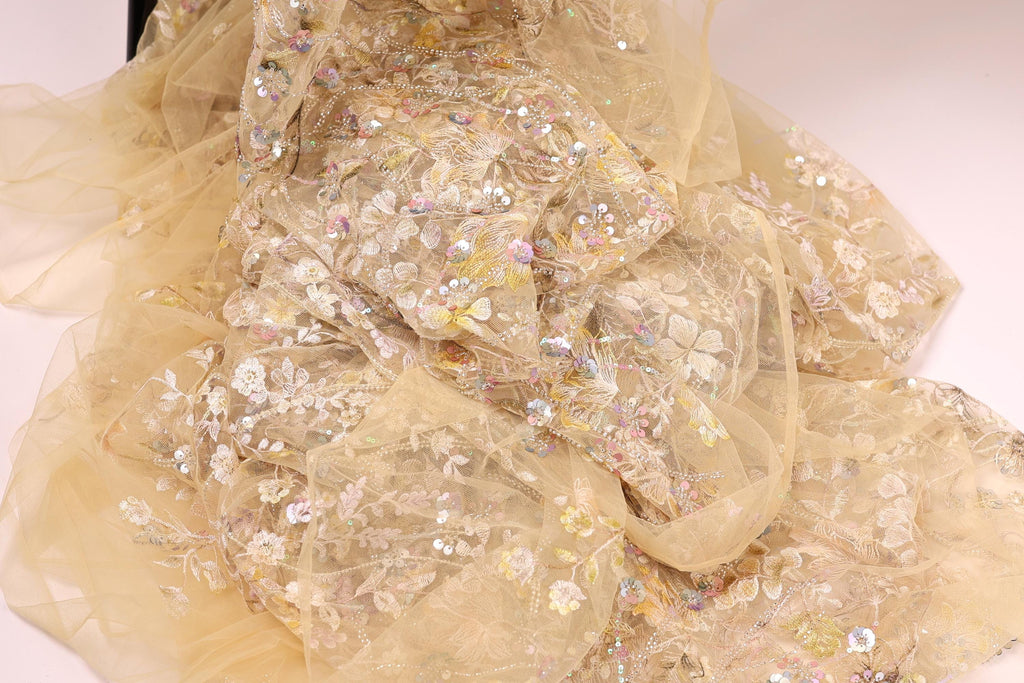 a close-up view of a delicate, intricately embroidered fabric with a floral pattern. The fabric appears to be made of sheer material, giving it a soft and delicate appearance. The embroidery features a variety of flowers and leaves, creating a visually appealing and detailed design.