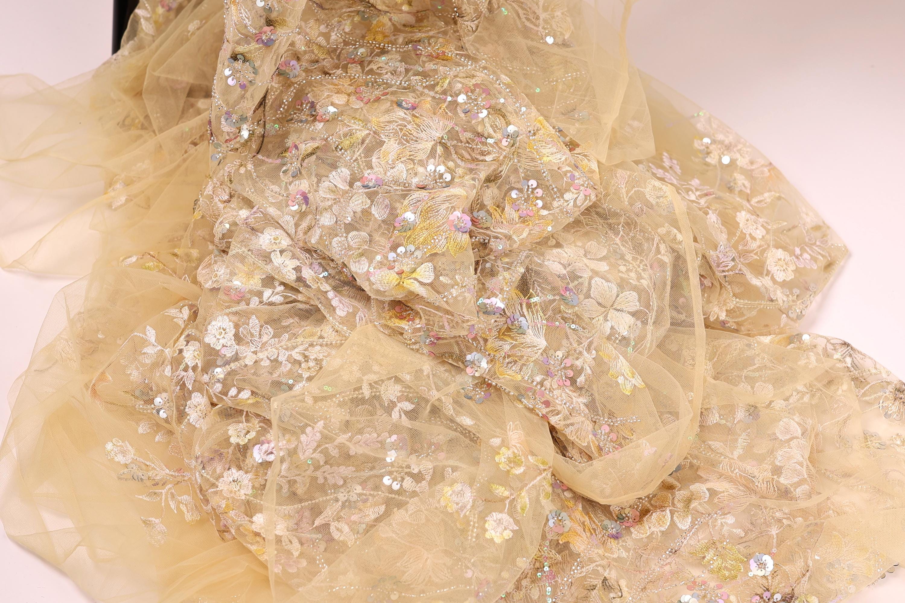 a close-up view of a delicate, intricately embroidered fabric with a floral pattern. The fabric appears to be made of sheer material, giving it a soft and delicate appearance. The embroidery features a variety of flowers and leaves, creating a visually appealing and detailed design.