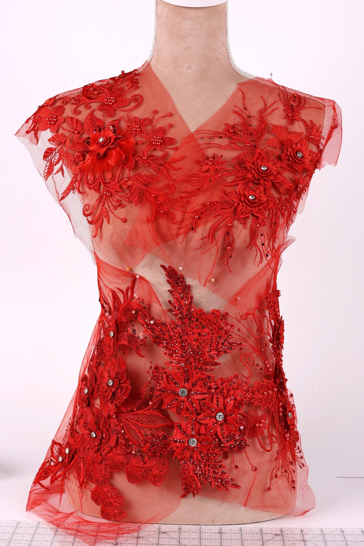 A mannequin wearing a red dress with intricate floral and leaf embroidery.