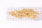 a decorative gold embroidered piece with intricate patterns and designs, including flowers and leaves, placed on a transparent ruler for scale.
