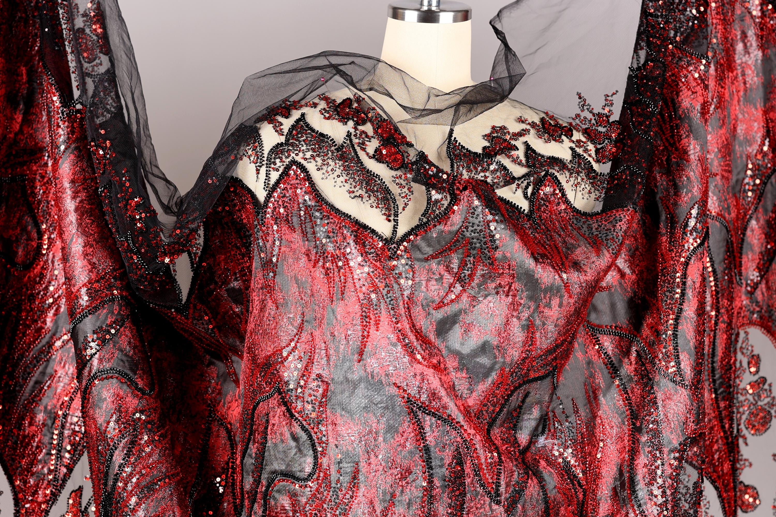 a red and black sequined dress with a sheer black overlay, displayed on a mannequin.