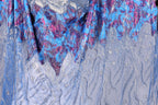 a close-up view of a fabric with a vibrant, colorful pattern. The fabric appears to be a blend of blue, purple, and white colors, with intricate designs and textures. The fabric is draped over a surface, creating a visually striking and eye-catching display.