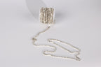 A silver-colored, sparkling chain is lying on a white surface, with its ends dangling in a loose, tangled manner.