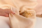 A hand is holding a piece of fabric, which appears to be a light-colored material. The fabric is folded and crumpled, suggesting it might be used for a craft or a decorative purpose.