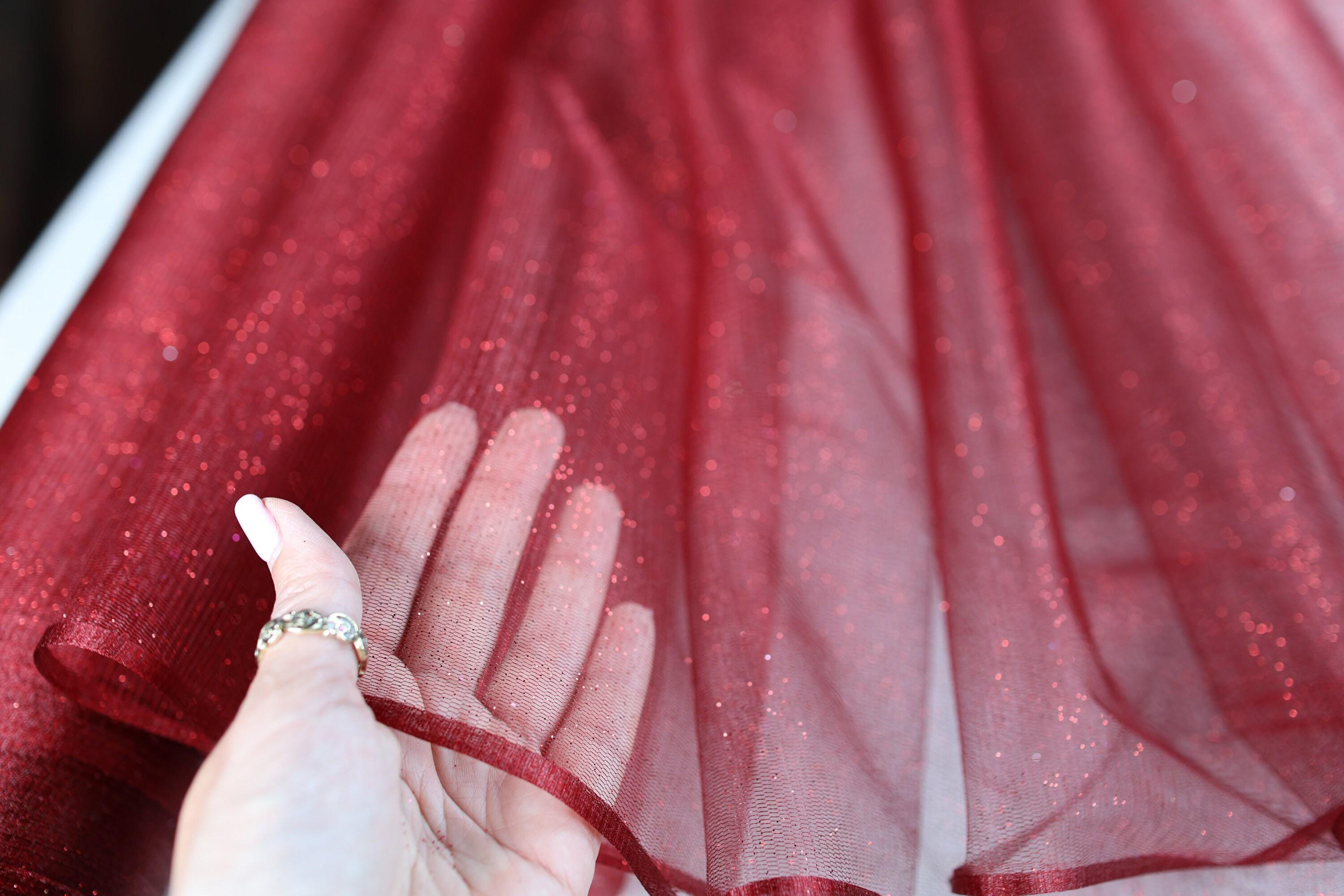 a woman's hand holding a red sheer curtain