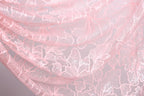 a close-up view of a delicate, pink lace fabric with a floral pattern. The lace appears to be made of a soft, delicate material and has a delicate, intricate design.