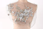 a mannequin with a delicate, intricate floral embroidery on its chest area. The embroidery is composed of silver and white flowers and leaves, creating a beautiful and elegant design. The mannequin is positioned against a plain white background, allowing the embroidery to stand out prominently.