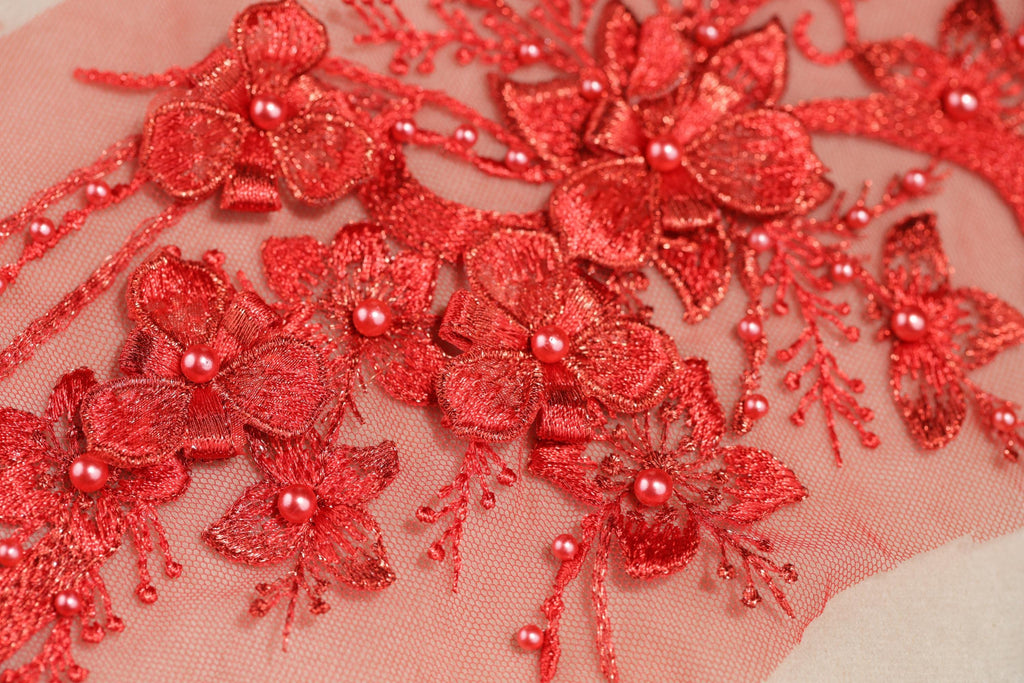 a close-up view of a delicate, intricate red embroidered design with numerous small flowers and pearls.