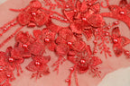 a close-up view of a delicate, intricate red embroidered design with numerous small flowers and pearls.