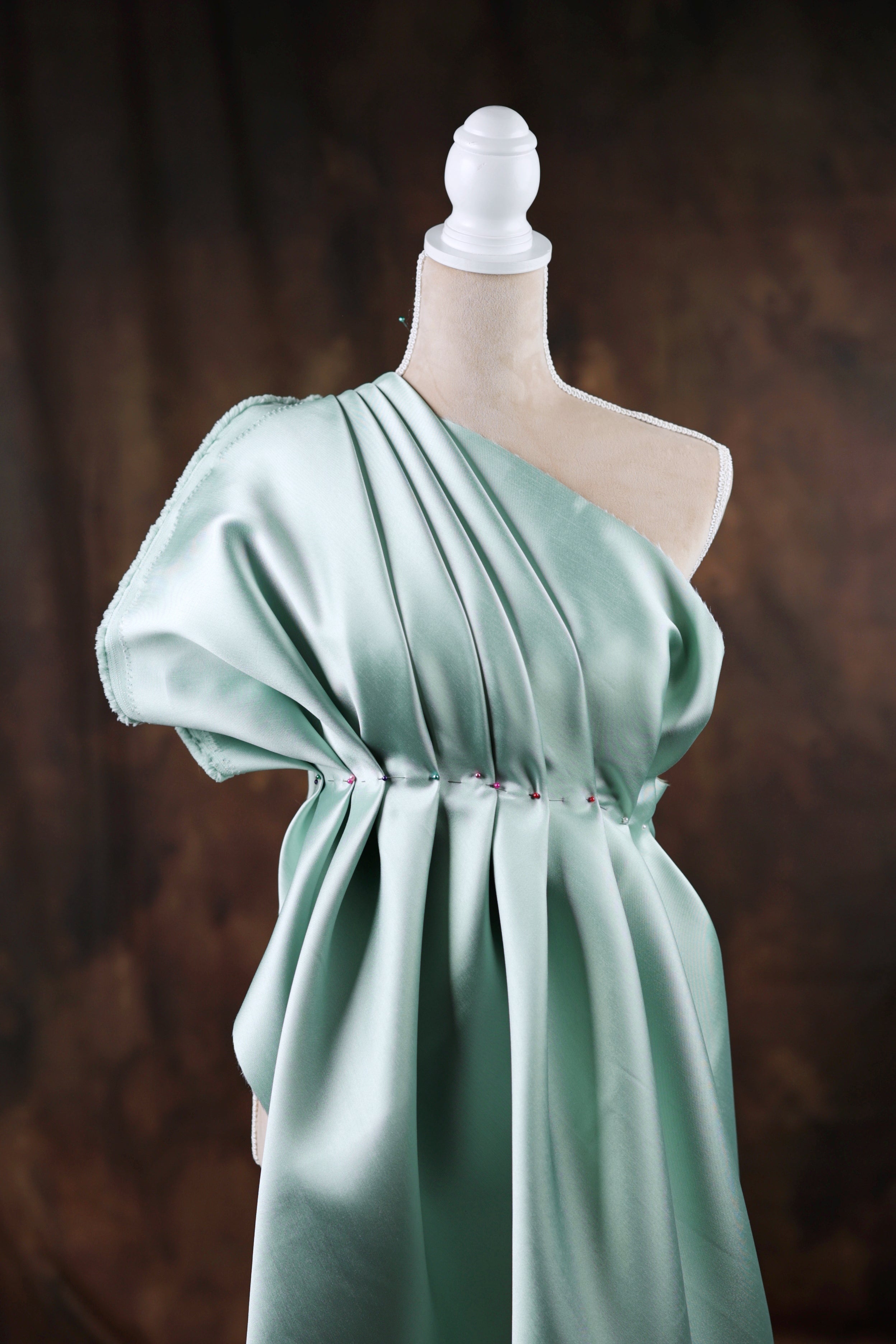 A mannequin wearing a one-shoulder dress with a draped, flowing green fabric.