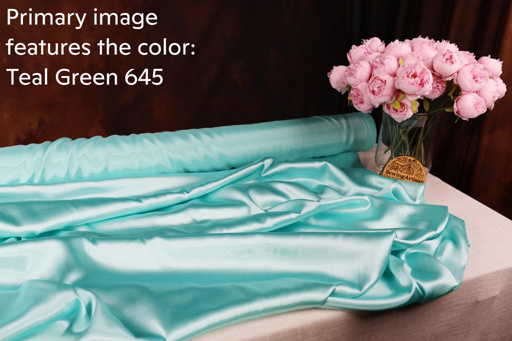 a roll of turquoise satin fabric and a vase of pink roses on a table.