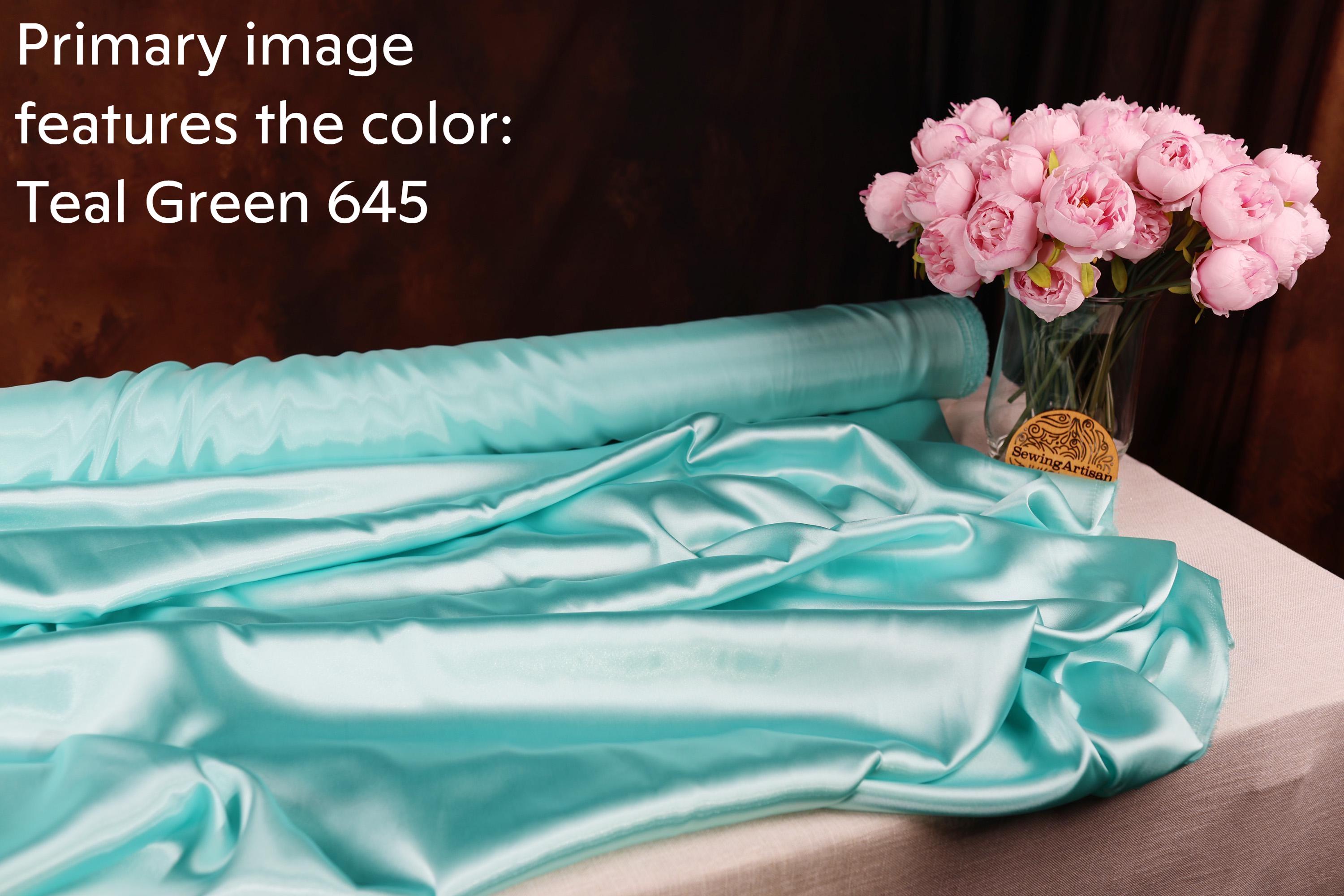 a roll of turquoise satin fabric and a vase of pink roses on a table.
