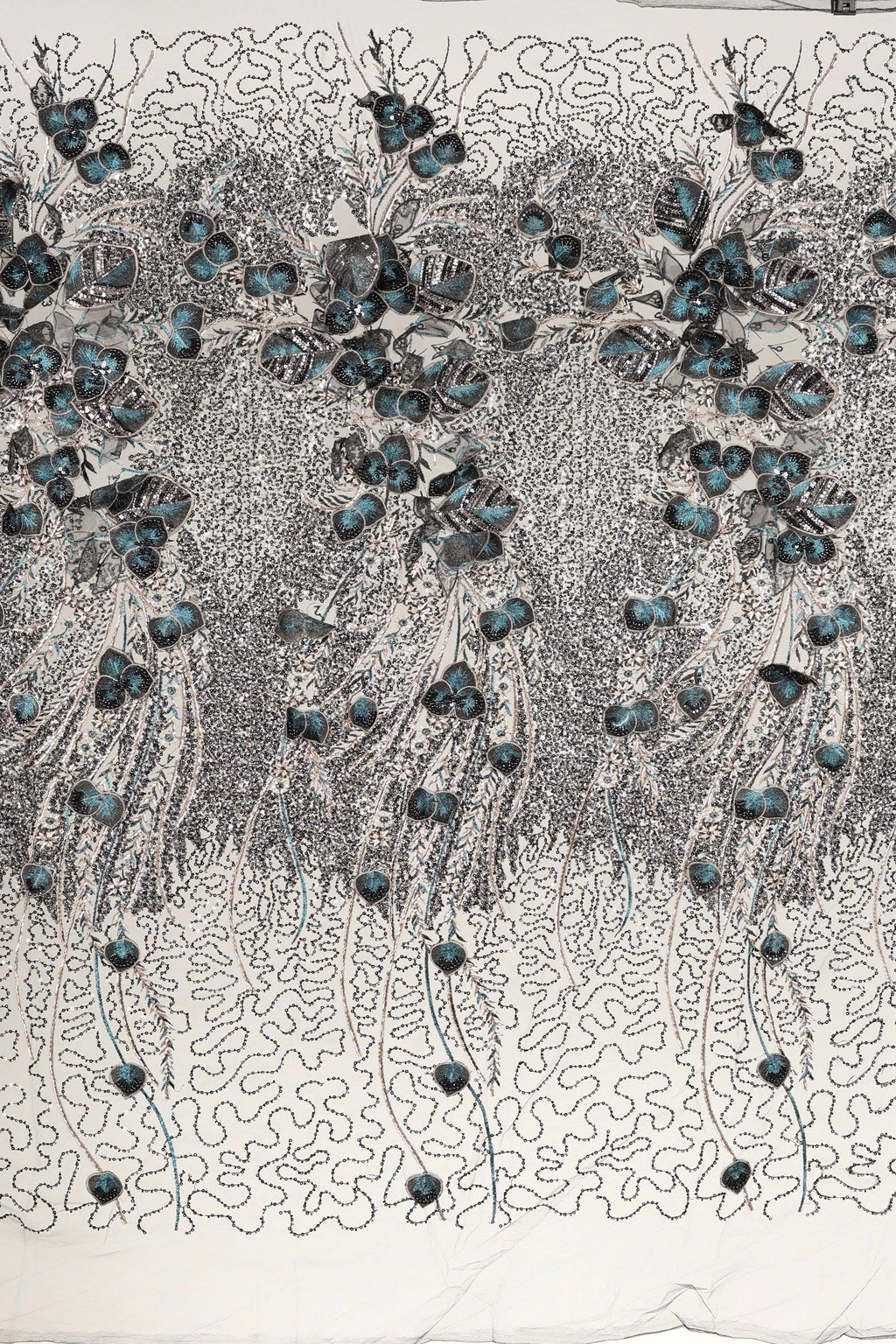 The image is a close-up of a fabric with a floral pattern, featuring a repeating design of blue flowers and leaves. The fabric appears to be made of a material with a textured surface, and the pattern is intricate and detailed.