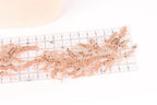 a close-up view of a delicate, intricate piece of embroidery or lace with a floral pattern. The piece is placed on a ruler, which is placed on a white surface.
