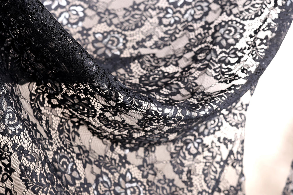 a close-up view of a black lace fabric with intricate floral patterns. The fabric appears to be made of a delicate, lace-like material, with a black and white color scheme. The close-up perspective allows for a detailed examination of the fabric's texture and design.