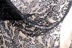 a close-up view of a black lace fabric with intricate floral patterns. The fabric appears to be made of a delicate, lace-like material, with a black and white color scheme. The close-up perspective allows for a detailed examination of the fabric's texture and design.