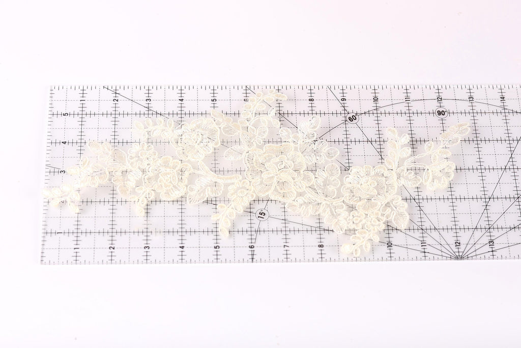 a close-up view of a piece of white lace with intricate floral patterns, placed on a transparent ruler.