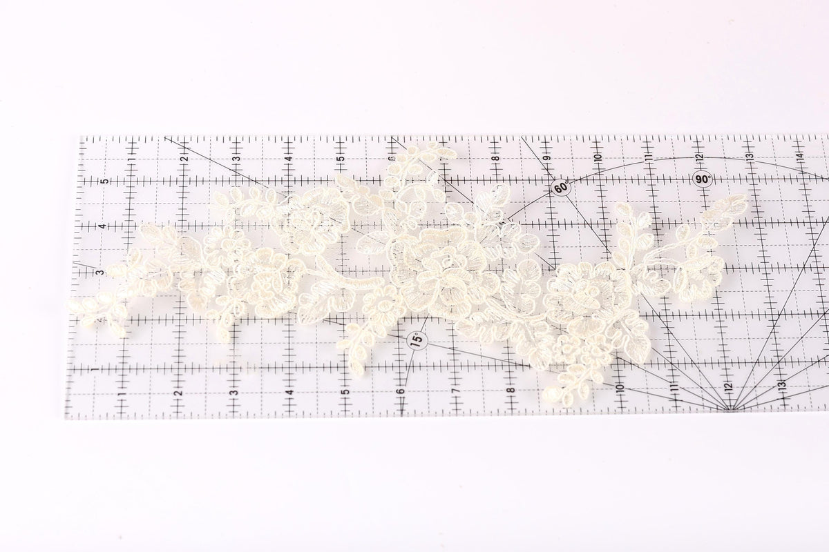 a close-up view of a piece of white lace with intricate floral patterns, placed on a transparent ruler.