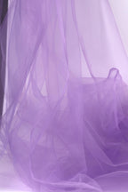 The image is a close-up of a soft, flowing purple fabric, possibly tulle, with a slightly crumpled texture.