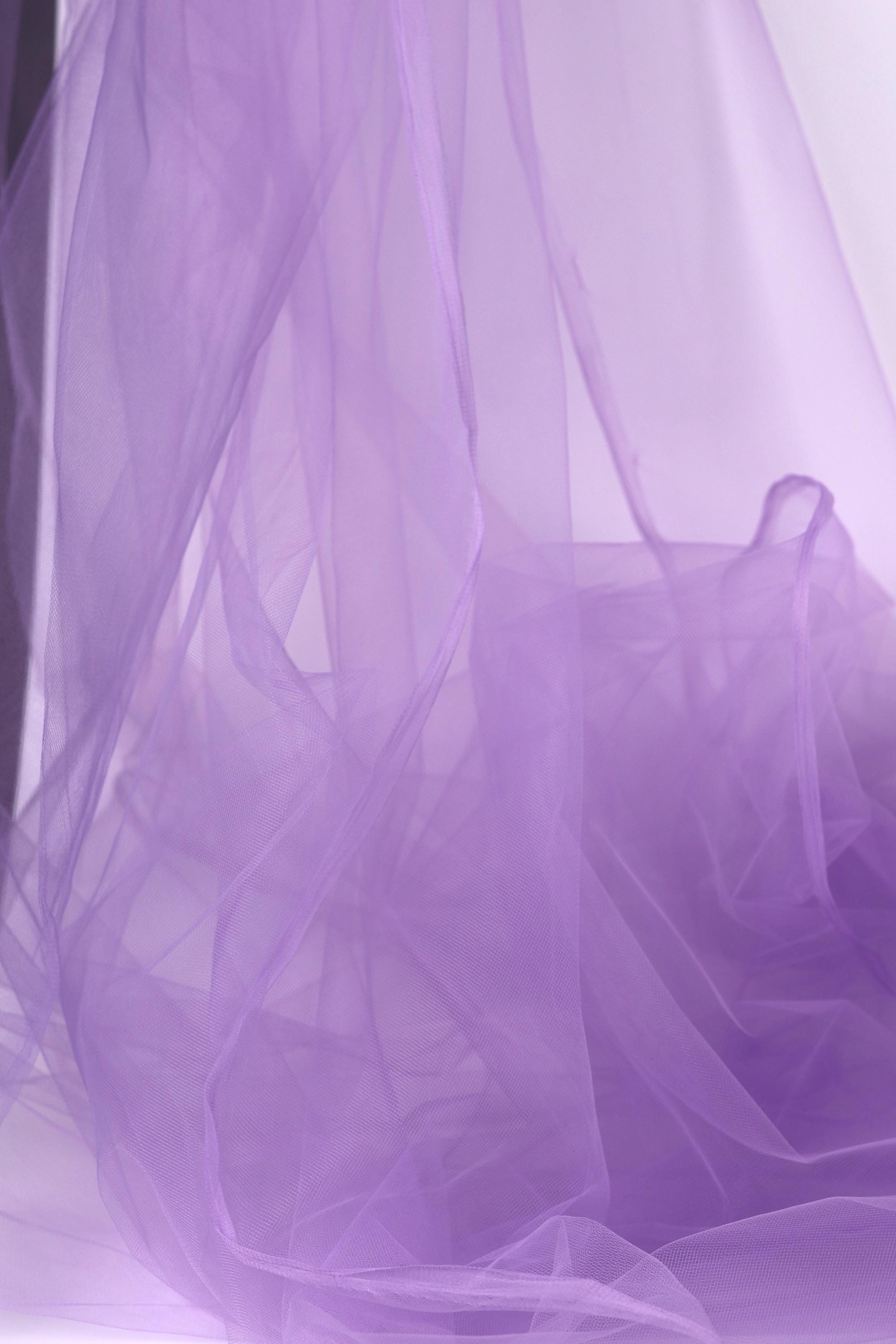 The image is a close-up of a soft, flowing purple fabric, possibly tulle, with a slightly crumpled texture.