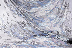 The image is a close-up of a fabric with a complex, swirling pattern of sequins in shades of blue, gray, and white. The fabric appears to be made of sheer material, giving it a delicate and ethereal appearance. The intricate design and the interplay of the different colors create a visually striking and captivating image.