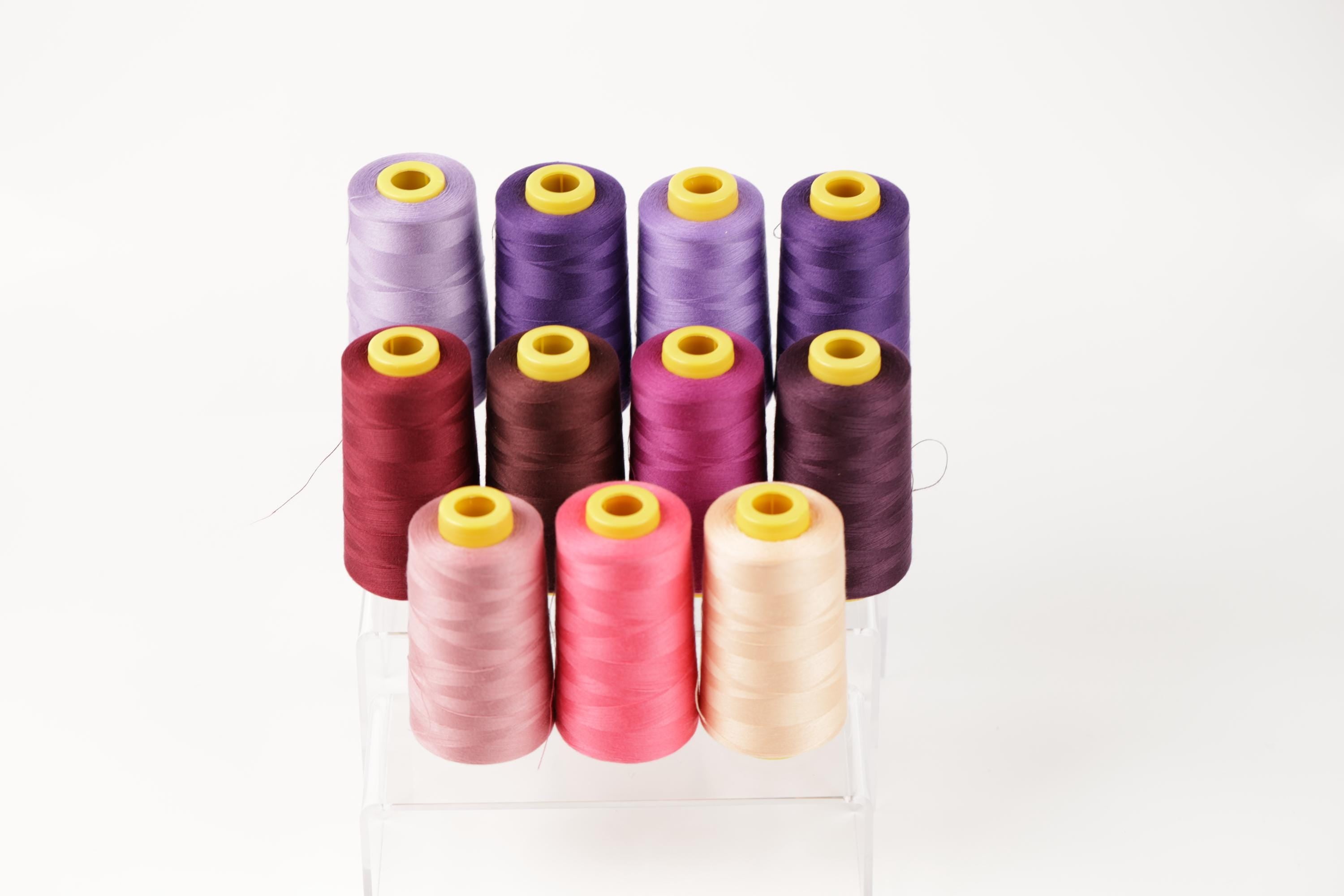 A collection of colorful spools of thread in various shades, including purple, pink, and yellow, arranged in a neat and organized manner.