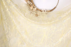 a close-up view of a delicate, yellow fabric with a floral pattern. The fabric appears to be made of sheer material, with a delicate and intricate design. The background is plain white, which allows the fabric and its details to stand out prominently.