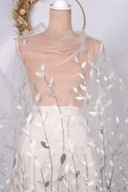 A mannequin wearing a white dress with a sheer, leaf-like fabric draped over it.
