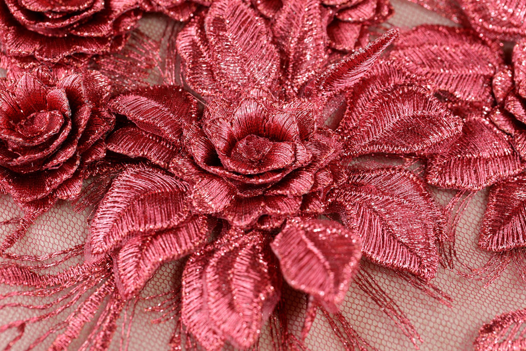 a close-up view of a fabric with a metallic, shiny texture. The fabric features a pattern of red, metallic flowers or leaves, which appear to be made of a shiny material. The fabric is spread across the entire frame, creating a visually striking and intricate design.