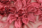 a close-up view of a fabric with a metallic, shiny texture. The fabric features a pattern of red, metallic flowers or leaves, which appear to be made of a shiny material. The fabric is spread across the entire frame, creating a visually striking and intricate design.