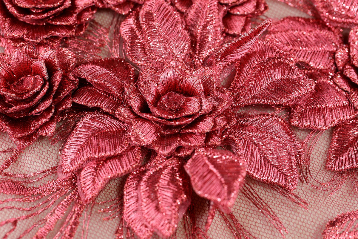 a close-up view of a fabric with a metallic, shiny texture. The fabric features a pattern of red, metallic flowers or leaves, which appear to be made of a shiny material. The fabric is spread across the entire frame, creating a visually striking and intricate design.
