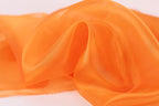 a close-up view of a soft, orange fabric, possibly silk or chiffon, with a smooth and flowing texture.