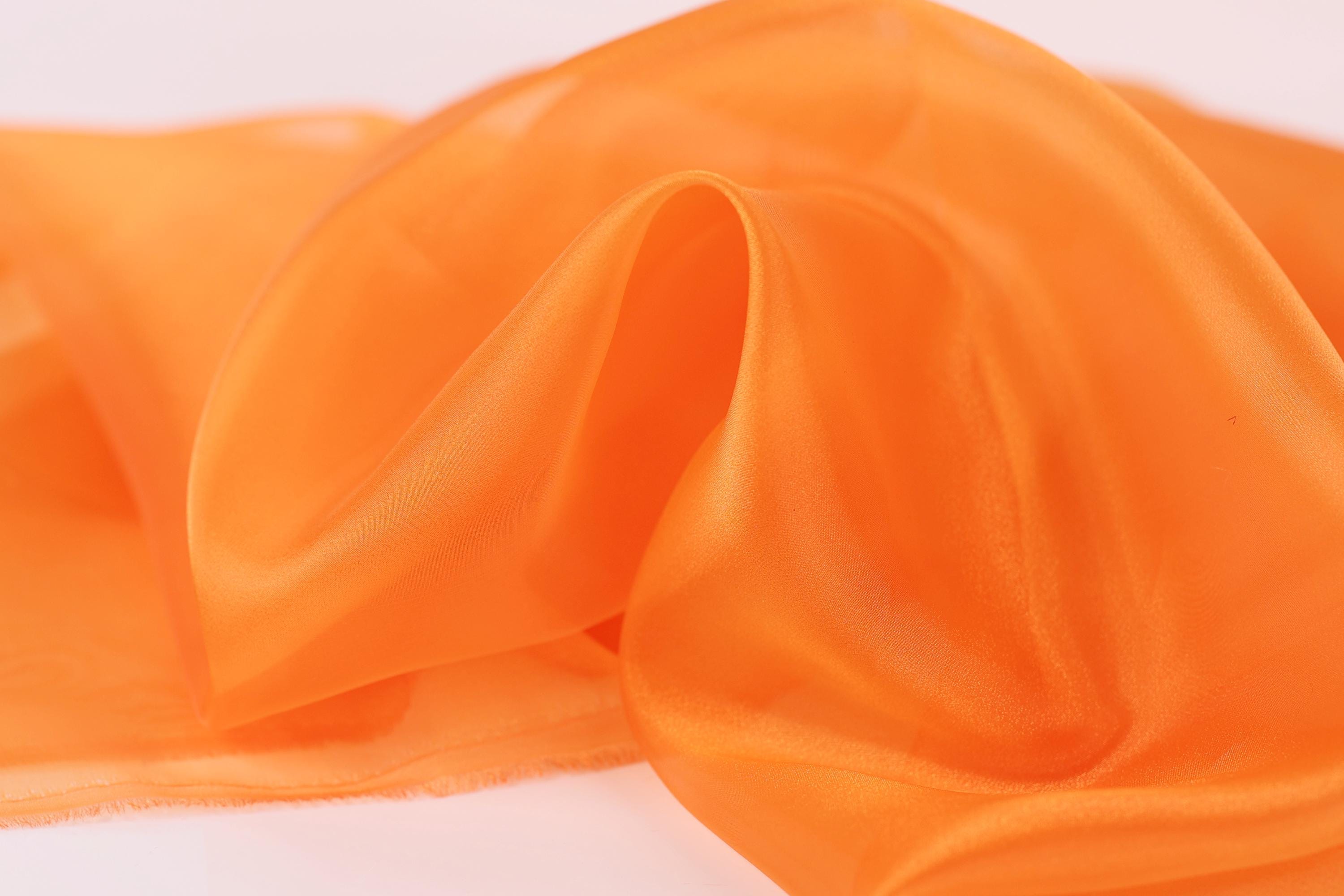 a close-up view of a soft, orange fabric, possibly silk or chiffon, with a smooth and flowing texture.