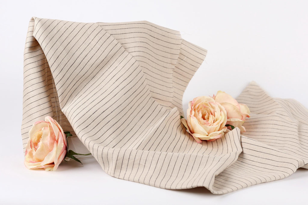 two pink roses resting on a beige fabric with black stripes.